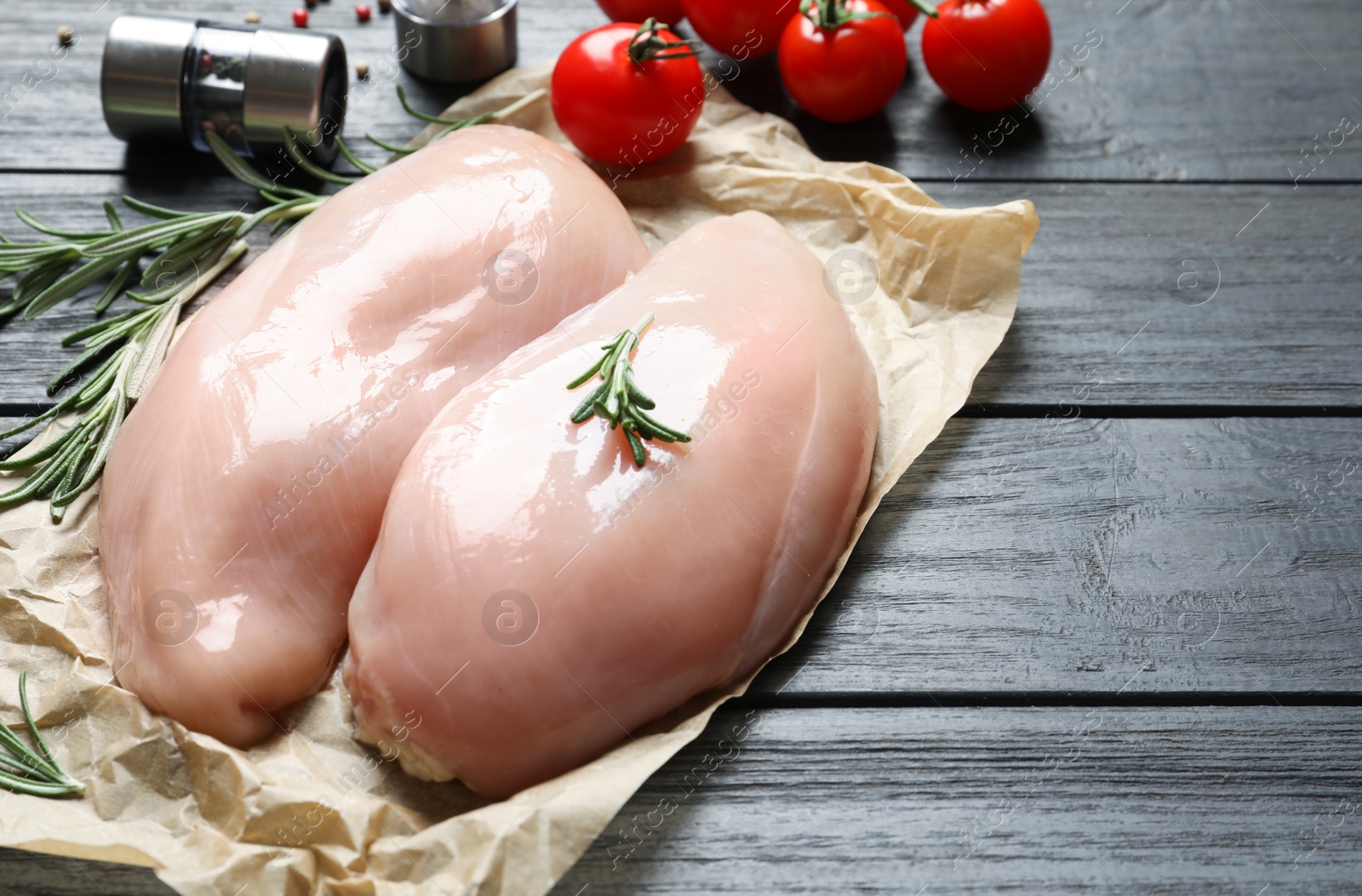 Photo of Parchment with raw chicken breasts and rosemary on wooden table. Space for text