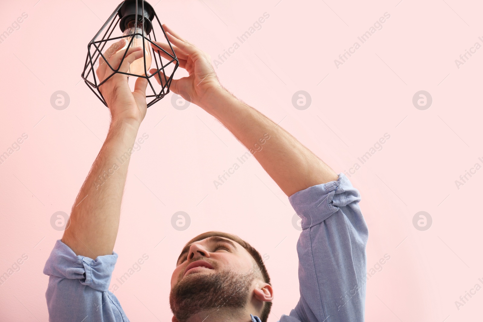 Photo of Man changing light bulb in lamp on color background