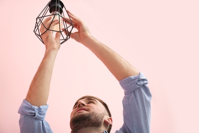 Man changing light bulb in lamp on color background