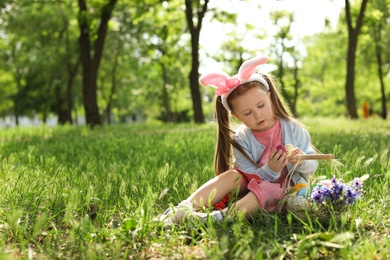 Photo of Little girl with bunny ears and basket full of Easter eggs outdoors
