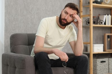 Photo of Overwhelmed man with glasses sitting in armchair at home