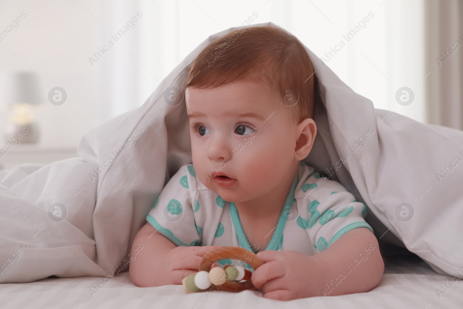 Photo of Cute little baby with toy in bed under soft blanket indoors