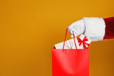 Santa holding paper bag with gift boxes on orange background, closeup. Space for text