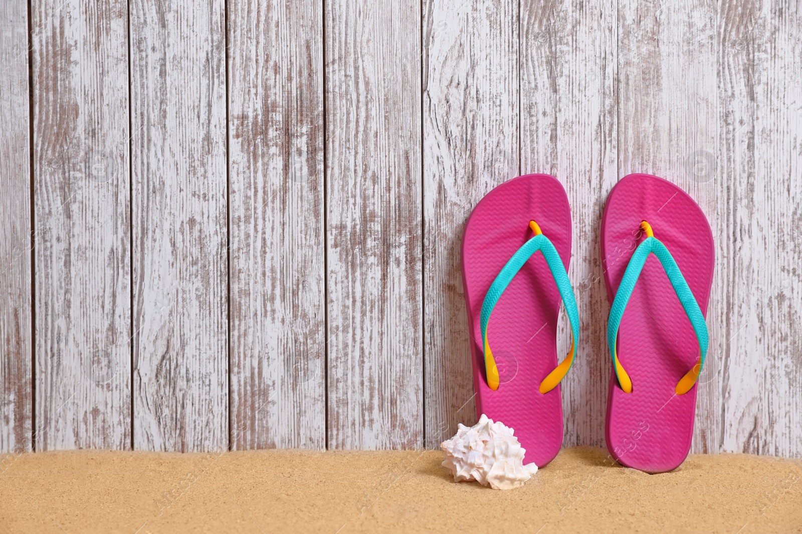 Photo of Flip flops and seashell on sand near wooden wall, space for text. Summer beach accessories