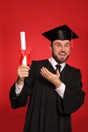 Happy student with graduation hat and diploma on red background