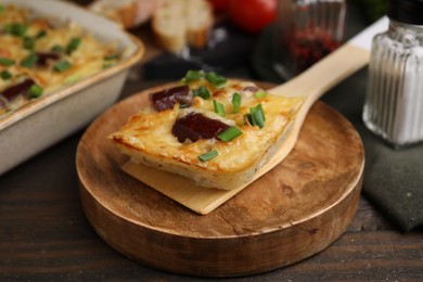 Photo of Spatula with piece of tasty sausage casserole on wooden table, closeup