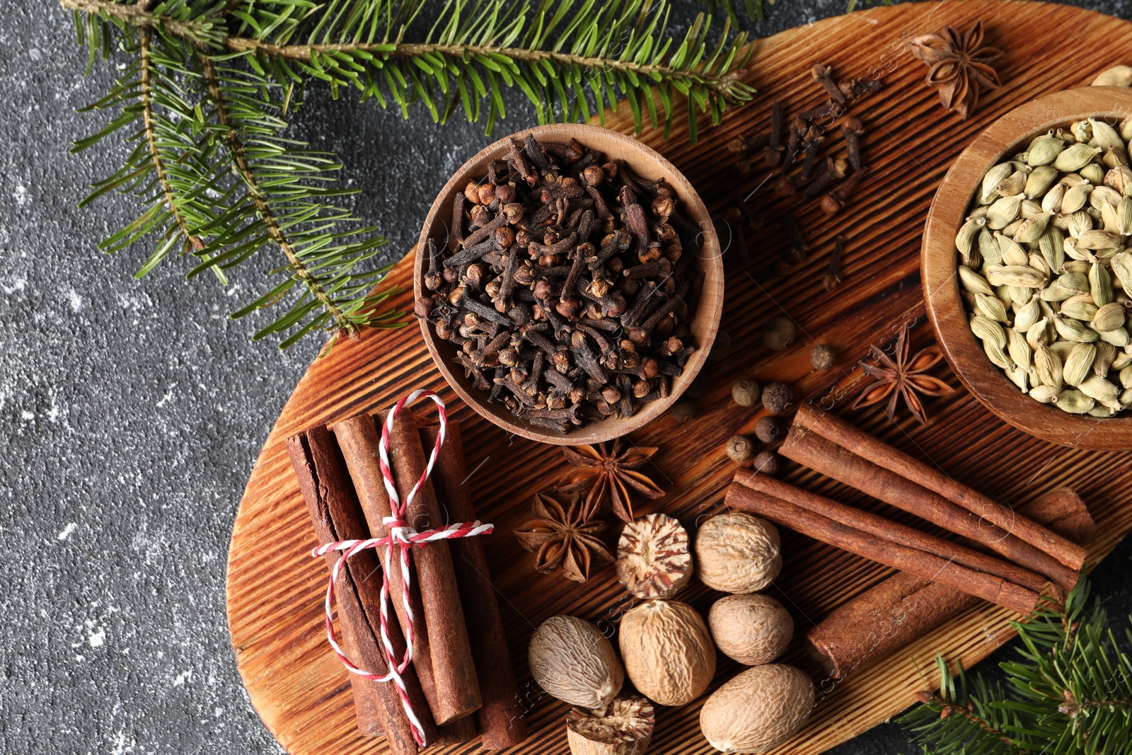 Photo of Different spices and fir branches on dark gray textured table, flat lay