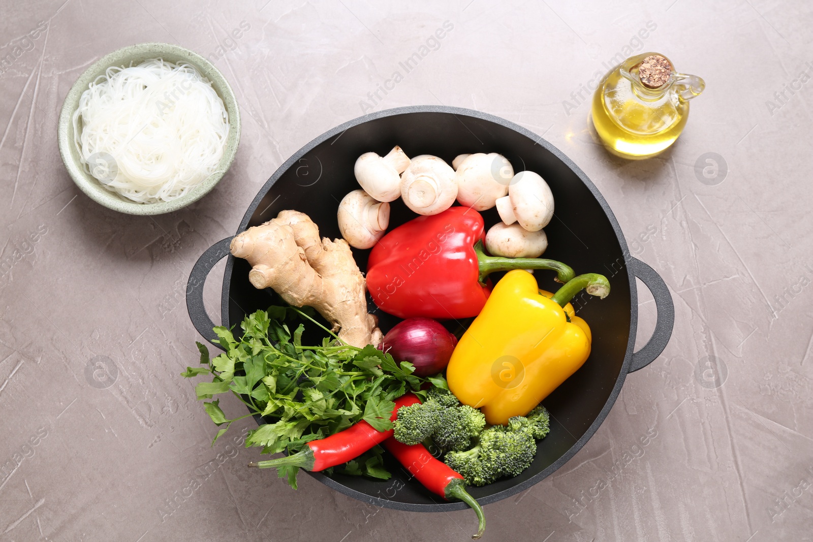 Photo of Wok, chopsticks and different products on grey textured table, flat lay