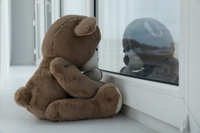 Photo of Cute lonely teddy bear on windowsill indoors