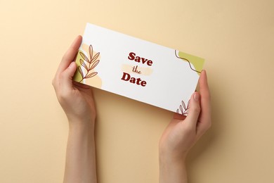 Photo of Woman holding beautiful card with Save the Date phrase on beige background, top view
