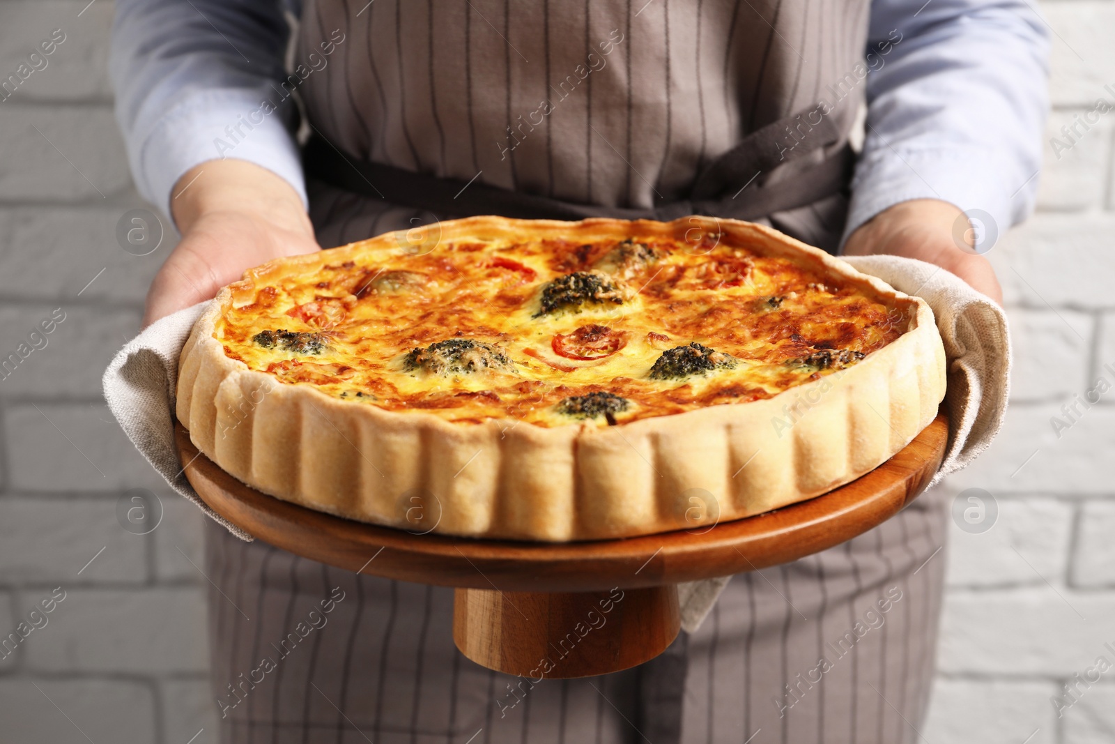 Photo of Woman holding delicious homemade vegetable quiche indoors, closeup