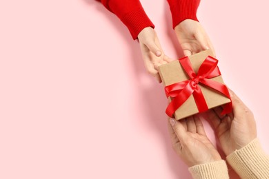 Photo of Mother giving gift box to her child on pink background, top view. Space for text