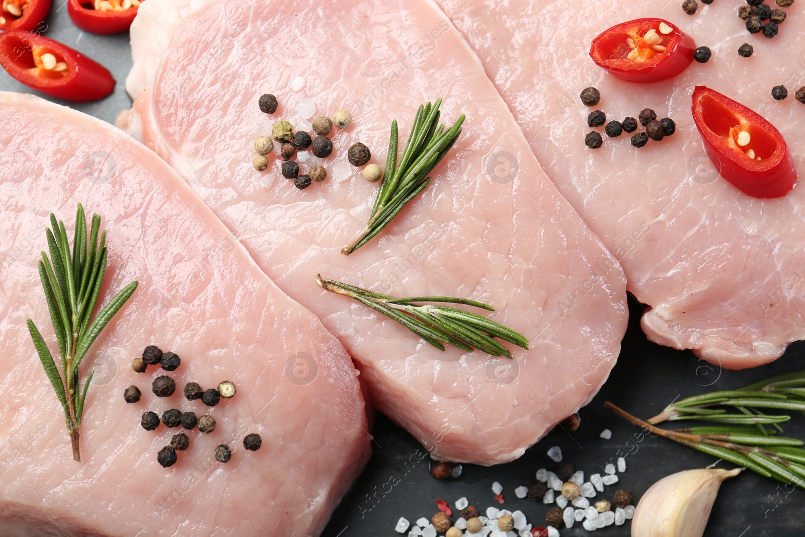 Photo of Pieces of raw pork meat, chili pepper and spices on board, closeup