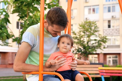 Photo of Father with adorable little baby on swing outdoors. Happy family