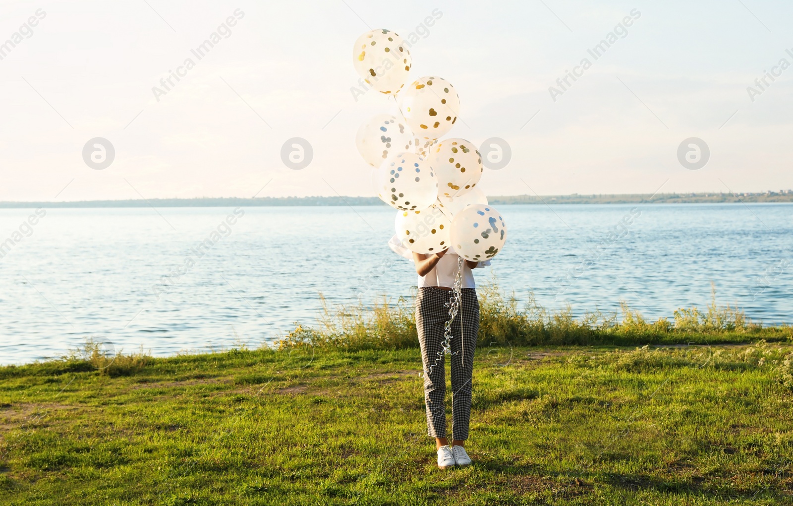 Photo of Beautiful young woman holding glitter balloons on riverside