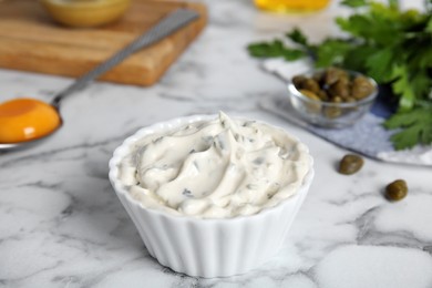 Photo of Tasty tartar sauce and ingredients on white marble table