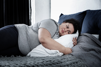Image of Depressed overweight woman lying alone on bed at home. Autophobia - fear of isolation