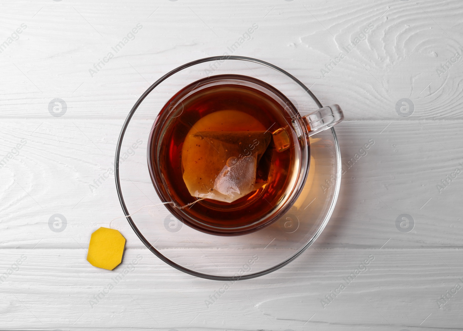 Photo of Tea bag in glass cup on white wooden table, top view