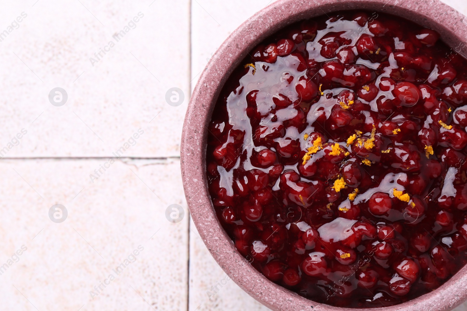 Photo of Tasty cranberry sauce in bowl on white tiled table, top view. Space for text