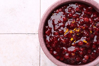 Photo of Tasty cranberry sauce in bowl on white tiled table, top view. Space for text