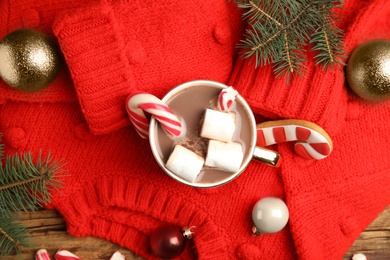 Photo of Flat lay composition with cup of tasty cocoa, candy cane and Christmas decor on wooden table, flat lay