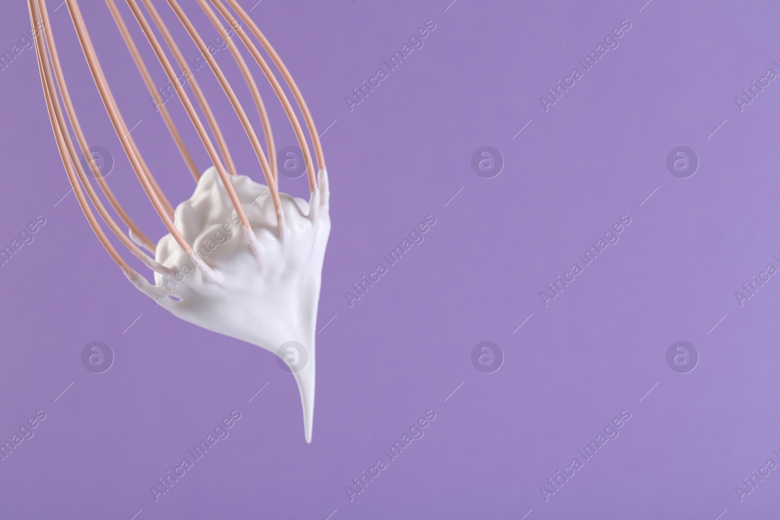 Photo of Whisk with whipped cream on violet background, closeup. Space for text