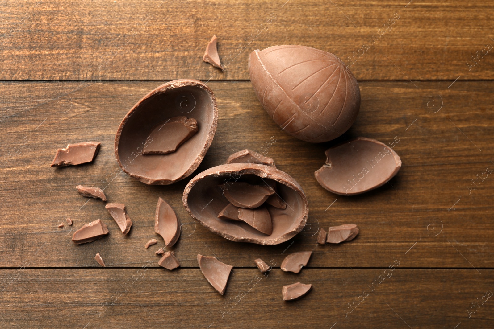 Photo of Broken chocolate eggs on wooden table, flat lay