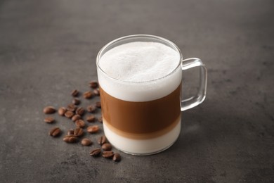 Hot coffee with milk in glass cup and beans on grey table