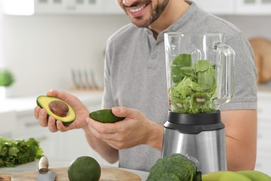 Photo of Man holding halves of avocado for delicious smoothie at table in kitchen, closeup