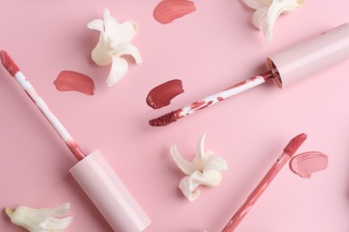 Different lip glosses, applicators and flowers on pink background, flat lay