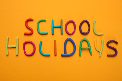 Photo of Phrase School Holidays made of modeling clay on orange background, top view