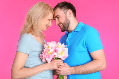 Photo of Young man congratulating his mature mom on color background. Happy Mother's Day