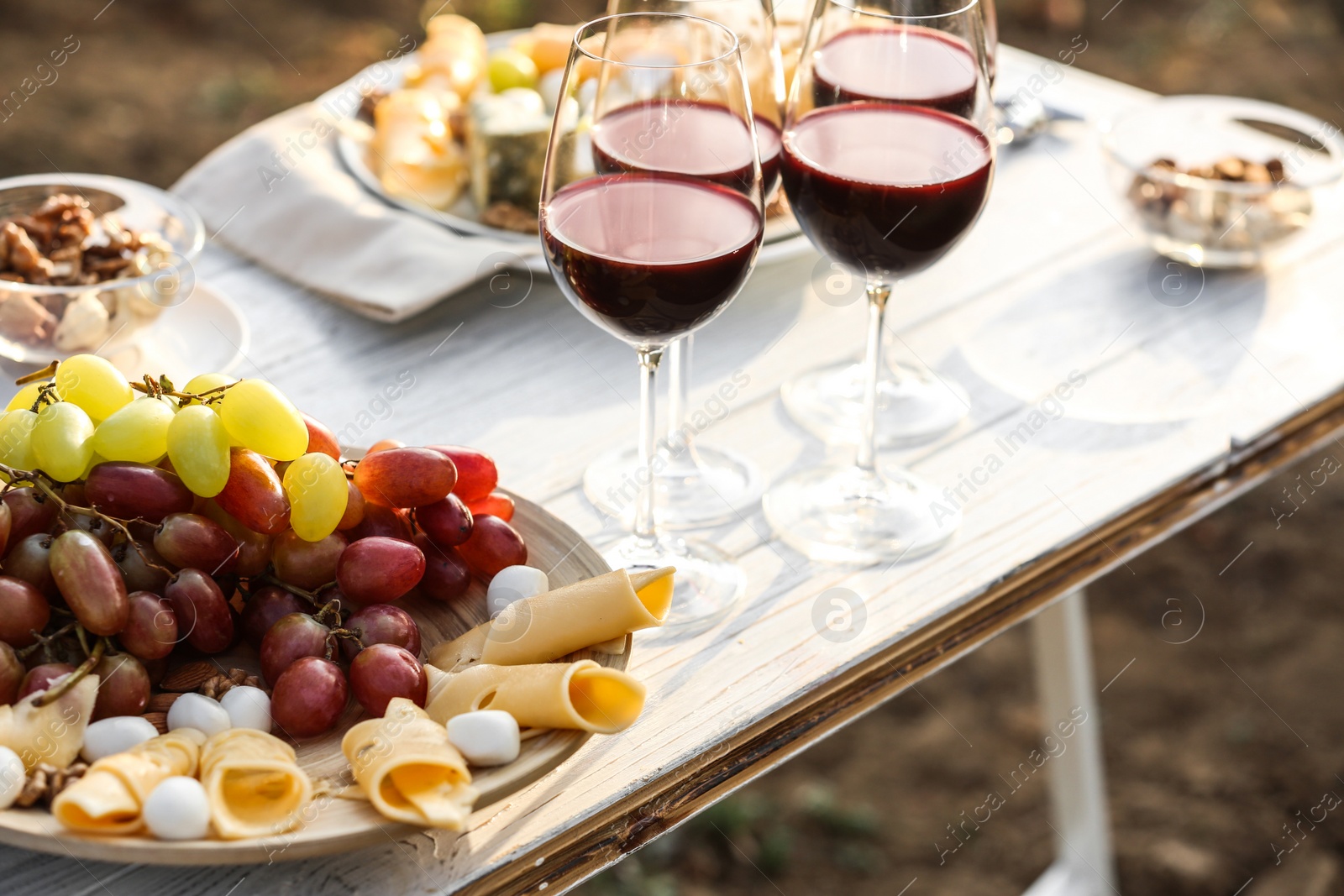 Photo of Red wine and snacks served for picnic on white wooden table outdoors