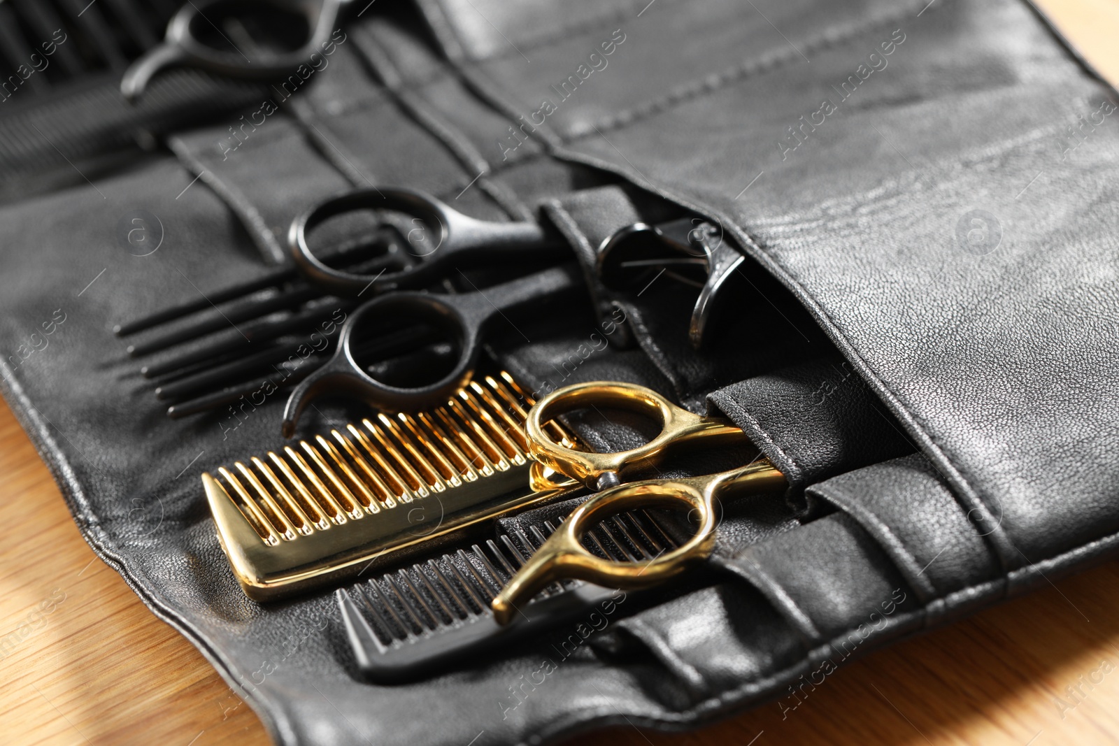 Photo of Hairdresser tools. Professional scissors and combs in leather organizer on wooden table, closeup