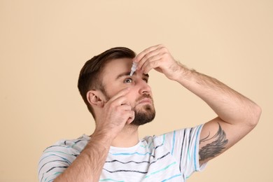 Photo of Young man using eye drops on beige background