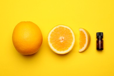 Photo of Bottle of citrus essential oil and fresh oranges on yellow background, flat lay