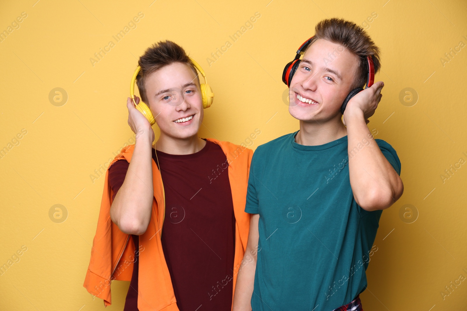 Photo of Teenage twin brothers with headphones on color background