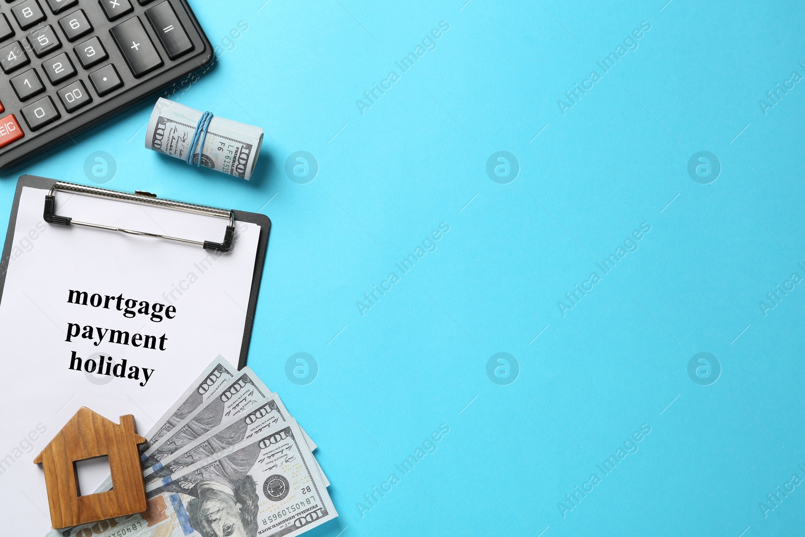 Photo of Clipboard with words Mortgage Payment Holiday, calculator, house model and money on light blue background, flat lay. Space for text