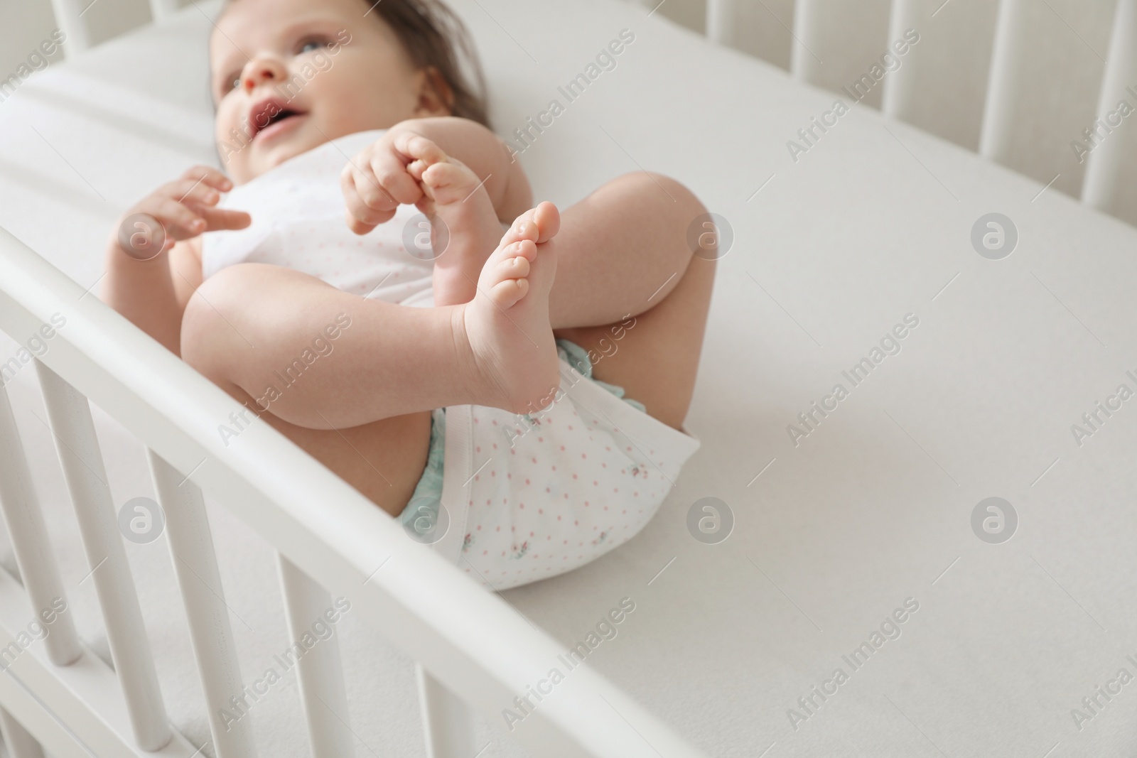 Photo of Cute little baby lying in comfortable crib at home, space for text