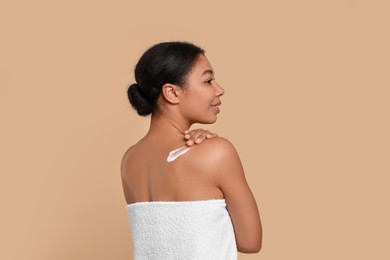 Photo of Young woman applying body cream onto back on beige background