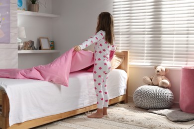Photo of Cute little girl making bed at home