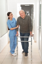 Photo of Nurse assisting senior patient with walker in hospital hallway