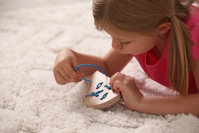 Photo of Cute little girl playing with wooden lacing toy on carpet indoors