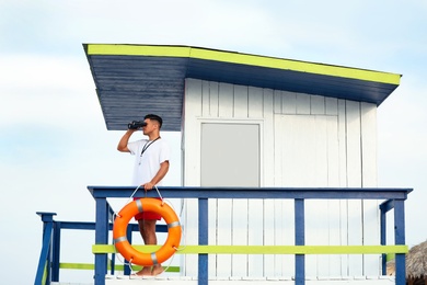 Photo of Male lifeguard with binocular on watch tower against blue sky
