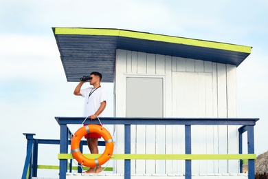 Male lifeguard with binocular on watch tower against blue sky