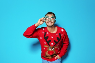 Photo of Young man in Christmas sweater with party glasses on color background