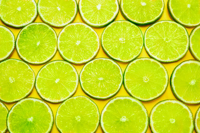 Photo of Juicy fresh lime slices on yellow background, flat lay