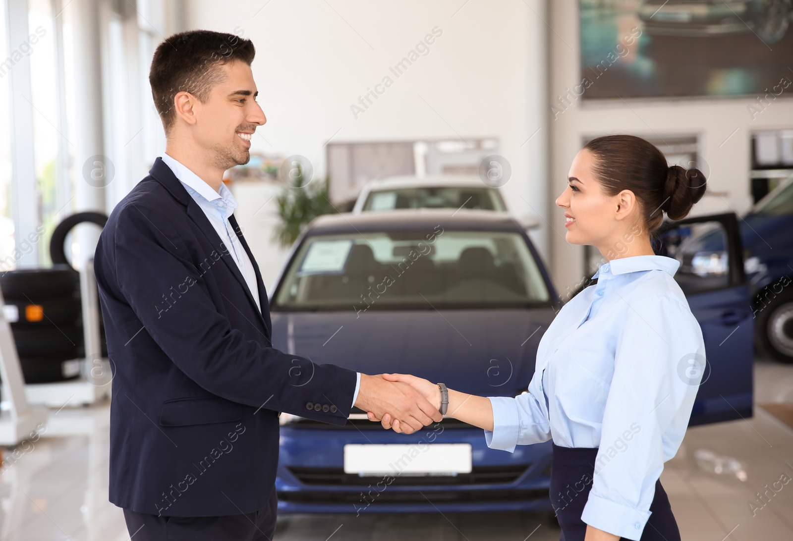 Photo of Young salesman working with client in car dealership