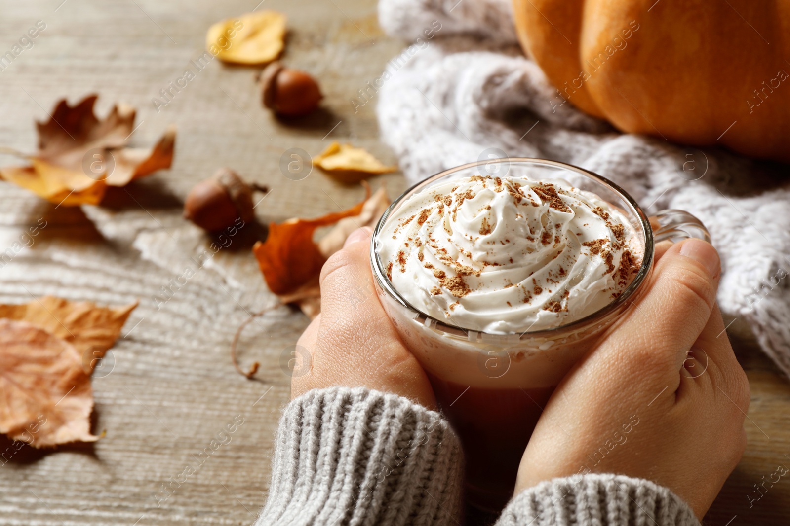 Photo of Woman with cup of pumpkin spice latte at wooden table, closeup