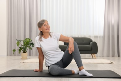 Photo of Happy senior woman sitting on mat at home. Yoga practice